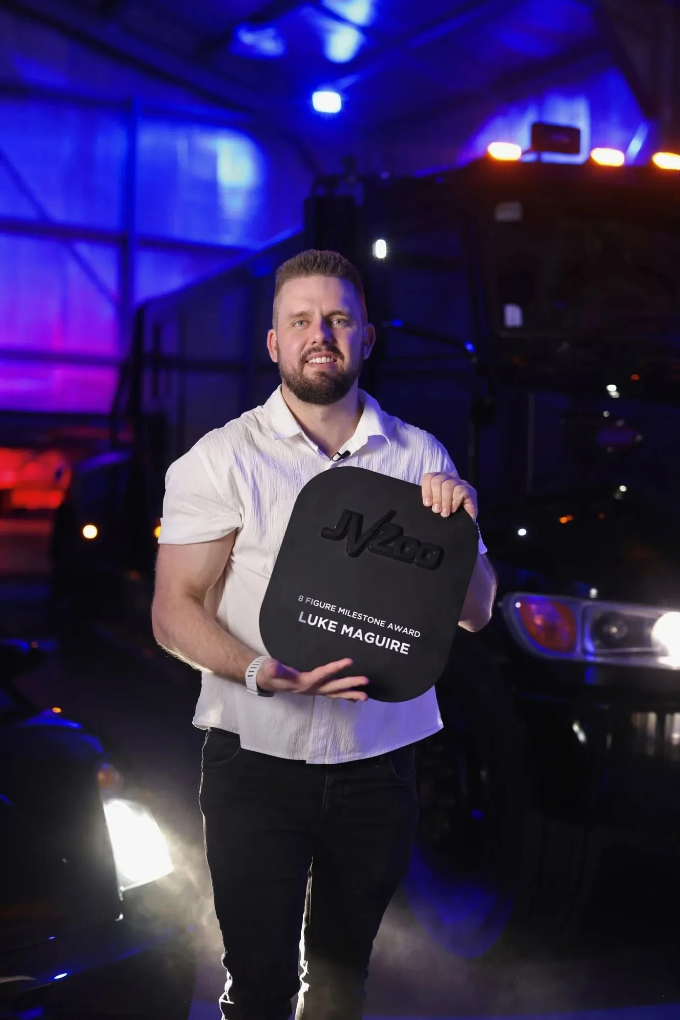 Luke Maguire holding the JVZoo 8 Figure Milestone Award in a neon-lit garage