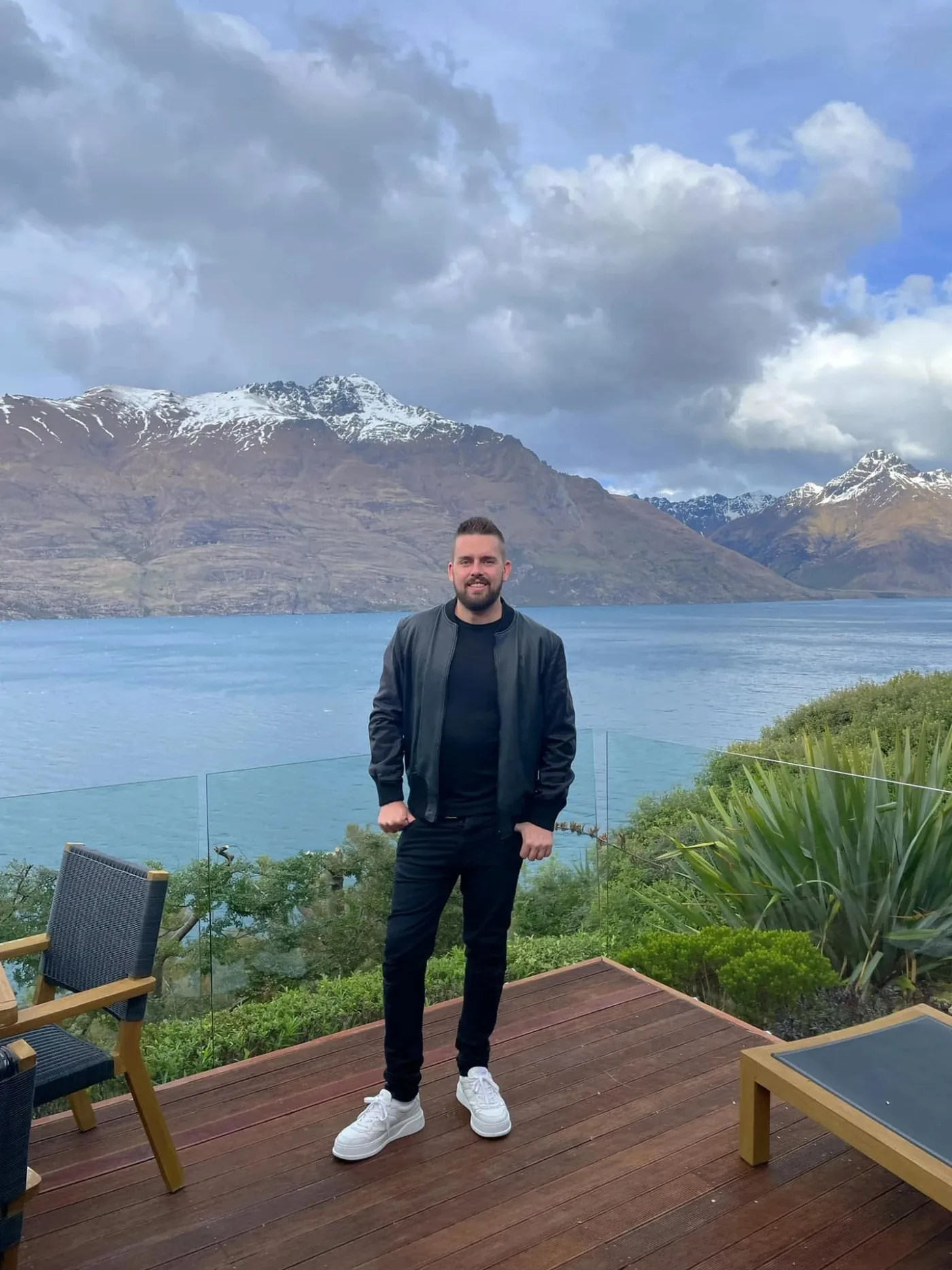 Luke on a deck above a lake in Queenstown with snowy mountains behind